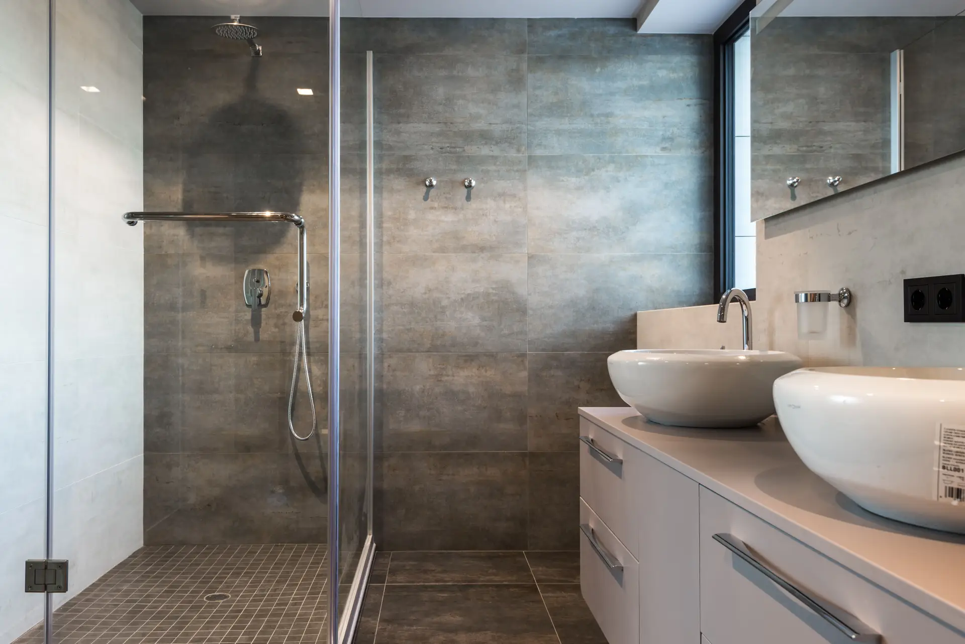 Bathroom with a glass shower enclosure, gray tile and two vessel sinks