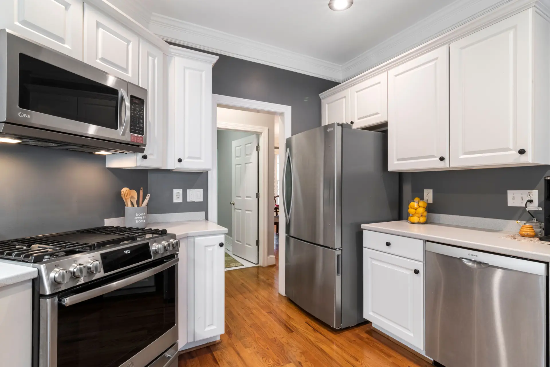 White kitchen with a dark backsplash, stainless steel appliances and wood floor